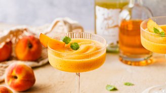 Ein erfrischender Pfirsich-Cocktail in einem eleganten Glas, garniert mit einem Pfirsichstück und frischer Minze.