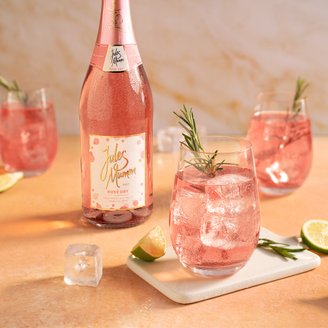 Ein eleganter Tisch mit einem Flasche Rosé und Gläsern, gefüllt mit pinkem Getränk, garniert mit Rosmarin und Limetten.