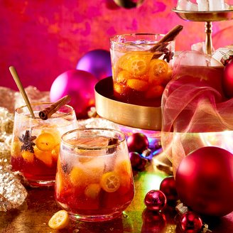 Bunte Cocktails in eleganten Gläsern, verziert mit Zimt und Zitrusfrüchten, vor einem leuchtend pinken Hintergrund.