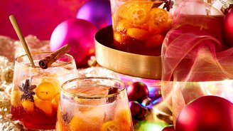 Bunte Cocktails in eleganten Gläsern, verziert mit Zimt und Zitrusfrüchten, vor einem leuchtend pinken Hintergrund.