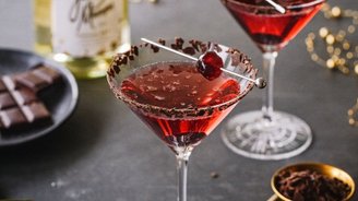 Zwei elegante Cocktails in Martinigläsern, dekoriert mit Schokoladenstückchen und einer Kirsche, stehen auf einem dunklen Tisch.
