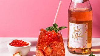Ein erfrischendes Getränk mit roten Beeren und Minze in einem eleganten Glas, umgeben von frischen Erdbeeren und einer Flasche Rosé.