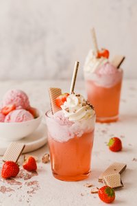 Ein erfrischendes Getränk mit rosa Eis, Sahne und frischen Erdbeeren, dekoriert mit Waffeln und einem goldenen Strohhalm.