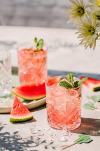 Zwei Gläser mit einem erfrischenden Wassermelonen-Cocktail, garniert mit frischer Minze, auf einem hellen Tisch.
