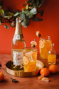 Ein eleganter Tisch mit einem goldenen Tablett, auf dem ein Glas mit einem fruchtigen Getränk und einer Flasche Sekt steht.