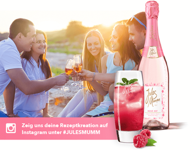 In einer entspannten Atmosphäre feiern Freunde mit Sekt und einem bunten Cocktail, während die Sonne untergeht.