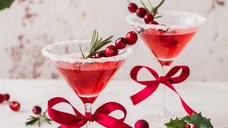 Zwei stilvolle Cocktails mit roten Schleifen, umgeben von festlichen Ornamenten und Tannenzweigen, strahlen Weihnachtsstimmung aus.