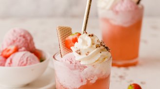 Ein erfrischendes Getränk mit rosa Eis, Sahne und frischen Erdbeeren, dekoriert mit Waffeln und einem goldenen Strohhalm.