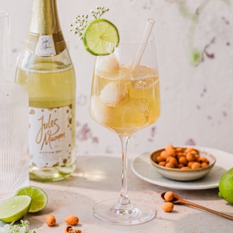 Ein stilvolles Getränk mit Eiswürfeln und Limette, dekoriert mit kleinen weißen Blüten, vor einer sanften, strukturierten Wand.