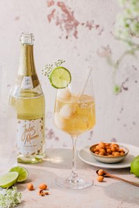 Ein stilvolles Getränk mit Eiswürfeln und Limette, dekoriert mit kleinen weißen Blüten, vor einer sanften, strukturierten Wand.