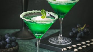 Zwei grüne Cocktails in eleganten Gläsern, dekoriert mit Minze und Zuckerrand, stehen auf einem dunklen Tisch.
