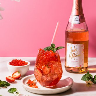 Ein erfrischendes Getränk mit roten Beeren und Minze in einem eleganten Glas, umgeben von frischen Erdbeeren und einer Flasche Rosé.