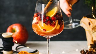 Auf einem Tisch stehen Gläser mit einem fruchtigen Getränk, umgeben von Tannenzweigen, getrockneten Orangen und Lichtern.