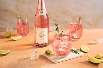 Ein eleganter Tisch mit einem Flasche Rosé und Gläsern, gefüllt mit pinkem Getränk, garniert mit Rosmarin und Limetten.