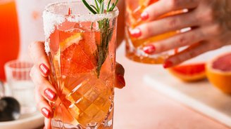 Zwei Gläser mit einem fruchtigen Getränk, garniert mit Rosmarin und Zitrusfrüchten, werden auf einem rosa Tisch serviert.