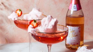 Zwei elegante Cocktails mit rosa Zuckerwatte und frischen Erdbeeren stehen auf einem marmorierten Tisch vor einer zarten rosa Wand.