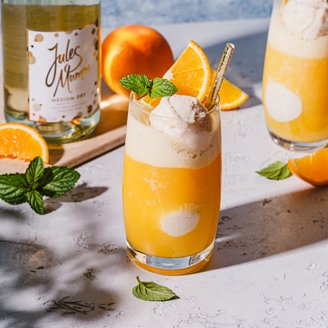 Zwei Gläser mit einem fruchtigen Cocktail, dekoriert mit einer Kugel Eis und frischen Minzblättern, auf einem hellen Tisch.