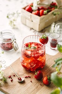 Ein erfrischendes Getränk mit frischen Erdbeeren und Minze, serviert in einem eleganten Glas auf einem Holzbrett.
