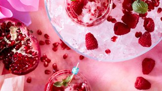 Drei Gläser mit gefrorenen Himbeeren und Granatapfelkernen auf Eis, umgeben von buntem Krepppapier.