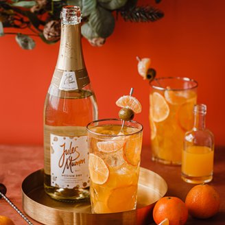 Ein eleganter Tisch mit einem goldenen Tablett, auf dem ein Glas mit einem fruchtigen Getränk und einer Flasche Sekt steht.