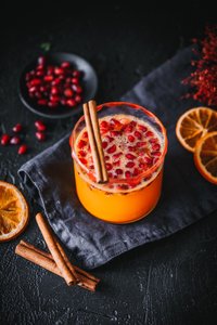 Ein leuchtend orangefarbener Drink mit Granatapfelkernen und Zimtstangen, umgeben von getrockneten Orangenscheiben.