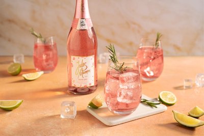 Ein eleganter Tisch mit einem Flasche Rosé und Gläsern, gefüllt mit pinkem Getränk, garniert mit Rosmarin und Limetten.