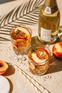 Zwei Gläser mit einem erfrischenden Getränk, garniert mit Pfirsichscheiben und Thymian, auf einem hellen Tisch.