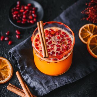 Ein leuchtend orangefarbener Drink mit Granatapfelkernen und Zimtstangen, umgeben von getrockneten Orangenscheiben.