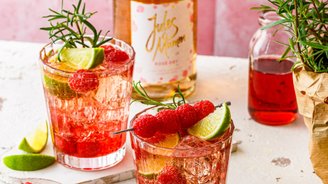 Fruchtige Cocktails mit Himbeeren und Limetten, serviert in eleganten Gläsern, umgeben von frischen Kräutern und einer Sektflasche.