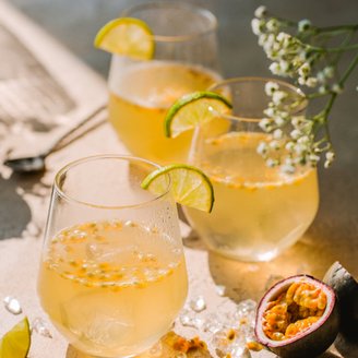 Erfrischende Getränke in eleganten Gläsern mit Limettenscheiben, umgeben von Eis und Passionsfrüchten auf einer rustikalen Oberfläche.