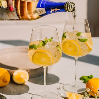Eine Hand gießt ein sprudelndes Getränk in ein Glas, während frische Zitronen und Minzblätter im Vordergrund liegen.