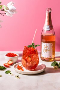 Ein erfrischendes Getränk mit roten Beeren und Minze in einem eleganten Glas, umgeben von frischen Erdbeeren und einer Flasche Rosé.