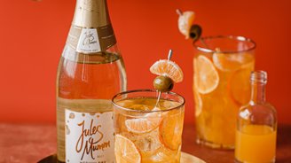 Ein eleganter Tisch mit einem goldenen Tablett, auf dem ein Glas mit einem fruchtigen Getränk und einer Flasche Sekt steht.