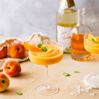 Ein erfrischender Pfirsich-Cocktail in einem eleganten Glas, garniert mit einem Pfirsichstück und frischer Minze.