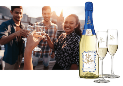 Ein Flasche Jules Mumm Sekt steht neben zwei Gläsern, während Freunde in einer entspannten Atmosphäre anstoßen.
