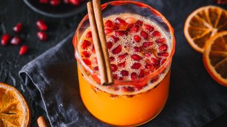 Ein leuchtend orangefarbener Drink mit Granatapfelkernen und Zimtstangen, umgeben von getrockneten Orangenscheiben.