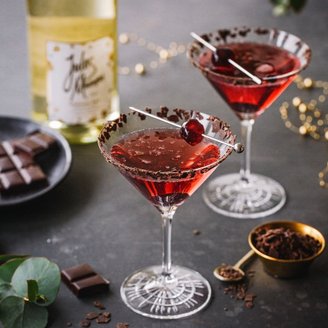 Zwei elegante Cocktails in Martinigläsern, dekoriert mit Schokoladenstückchen und einer Kirsche, stehen auf einem dunklen Tisch.