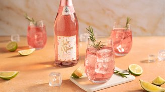 Ein eleganter Tisch mit einem Flasche Rosé und Gläsern, gefüllt mit pinkem Getränk, garniert mit Rosmarin und Limetten.