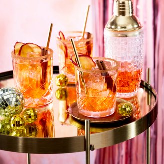 Drei Gläser mit bunten Cocktails, dekoriert mit Apfelscheiben und Zimtstangen, stehen auf einem goldenen Tisch.