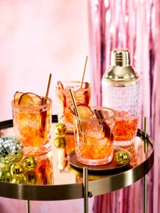 Drei Gläser mit bunten Cocktails, dekoriert mit Apfelscheiben und Zimtstangen, stehen auf einem goldenen Tisch.