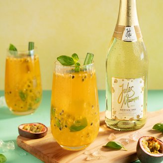Die Gläser enthalten ein fruchtiges Getränk mit Passionsfruchtstücken und Basilikum, während die Flasche Sekt im Hintergrund leuchtet.