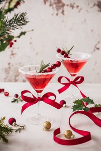 Zwei stilvolle Cocktails mit roten Schleifen, umgeben von festlichen Ornamenten und Tannenzweigen, strahlen Weihnachtsstimmung aus.