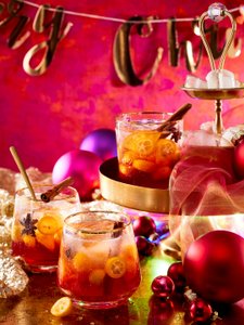 Festliche Getränke in Gläsern mit Eis und Zitrusfrüchten, umgeben von leuchtenden Weihnachtsornamenten und einer fröhlichen Atmosphäre.