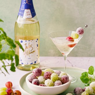 Ein stilvolles Martini-Glas mit sprudelndem Getränk und einer Garnitur aus bunten Trauben, neben einer Flasche Sekt platziert.