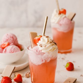 Ein erfrischendes Getränk mit rosa Eis, Sahne und frischen Erdbeeren, dekoriert mit Waffeln und einem goldenen Strohhalm.