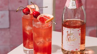 Auf einem weißen Tisch stehen zwei Cocktails mit Eis, dekoriert mit Kirschen und Grapefruit, neben einer Flasche Rosé.