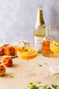 Ein erfrischender Pfirsich-Cocktail in einem eleganten Glas, garniert mit einem Pfirsichstück und frischer Minze.